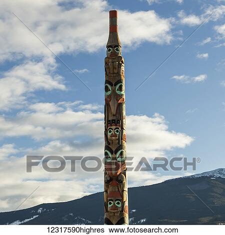 Totem pole against a blue sky with cloud and a mountain in the background, Jasper National park; Alberta, Canada View Large Photo Image Stock Photograph - Totem pole against a blue sky with cloud and a mountain in the background, Jasper National park; Alberta, Canada. Fotosearch