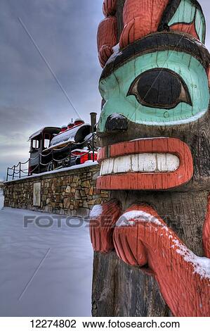 Stock Image - Totem pole and train at the Alaska Railroad Depot in Anchorage, Southcentral Alaska, HDR. Fotosearch