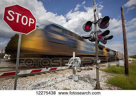 Train with blurred movement passing from right to left at a railroad crossing that has the safety gate down, stop sign, and flashing lights; United States of America View Large Photo Image Stock Photo - Train with blurred movement passing from right to left at a railroad crossing that has the safety gate down, stop sign, and flashing lights; United States of America. Fotosearch