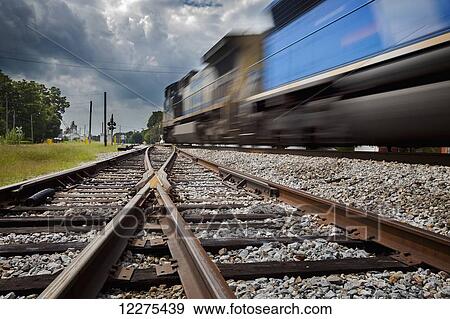Train with blurred movement with converging rails in the foreground and moody clouds in the sky; United States of America View Large Photo Image Stock Photo - Train with blurred movement with converging rails in the foreground and moody clouds in the sky; United States of America. Fotosearch