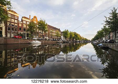 Stock Photo - Tranquil water reflecting buildings and trees in a canal, Singelgracht; Amsterdam, Netherlands. Fotosearch