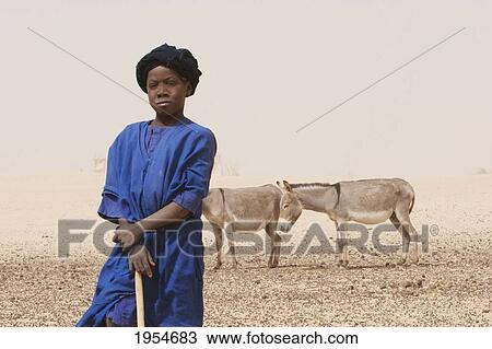 Stock Image - Tuareg boy standing with donkeys in the background, Nibka Mohammed, Mali. Fotosearch