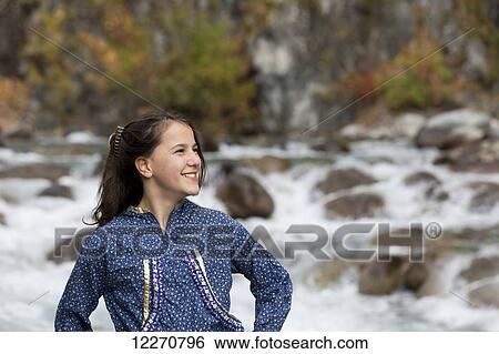 Stock Photograph - Tween Inupiat Eskimo girl in a traditional native kuspuk dress standing next to Little Susitna River, Hatcher Pass, Southcentral Alaska, Autumn. Fotosearch