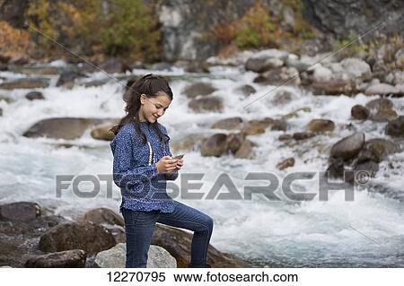 Stock Photography - Tween Inupiat Eskimo girl in a traditional native kuspuk dress texting with cell phone near Hatcher Pass, Southcentral Alaska, Autumn. Fotosearch