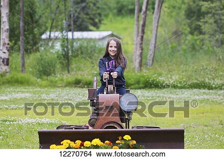 Picture - Tween Inupiat Eskimo girl sitting on an old tractor at the Knik Goose Bay Museum in Wasilla, Southcentral Alaska.. Fotosearch