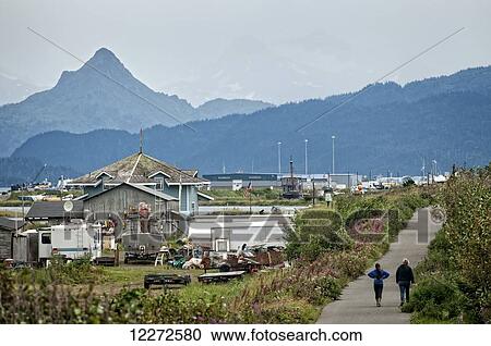 Stock Image - Two Homer residents walking on a path with Homer Spit and Poot Peak in the background, Kenai Peninsula, Southcentral Alaska, Autumn. Fotosearch