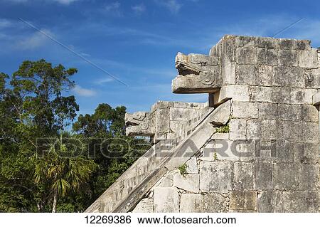 Stock Photograph - Two large Ancient Mayan stone carved Jaguar heads above stone steps to a platform with blue sky; Chichen Itza, Yucatan, Mexico. Fotosearch