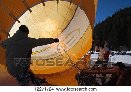 Picture - Two men hold open a hot air balloon while a third fires up the burner to inflate the balloon with hot air; Filzmoos, Austria. Fotosearch