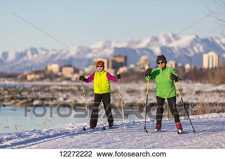 Stock Image - Two people cross country skiing on the Tony Knowles Coastal Trail with Anchorage in the background, Southcentral Alaska. Fotosearch