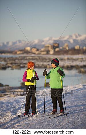 Stock Photography - Two people cross country skiing on the Tony Knowles Coastal Trail with Anchorage in the background, Southcentral Alaska. Fotosearch