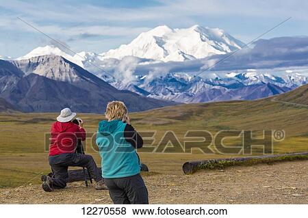 Stock Photo - Two tourists photograph Mt. McKinley and Thorofare Pass from Stony Dome in Denali National Park, Interior Alaska, Summer, USA.. Fotosearch