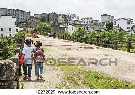 Stock Photo - Two young girls walking along the bridge in a small village near to Wuyuan; Jiangxi province, China. Fotosearch