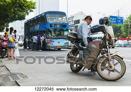 Stock Photography - Typical motorbike taxi and passengers getting on a bus on the road; Wuhan, Hubei province, China. Fotosearch