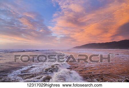 Stock Photograph - Vibrant red sunset over Cobden beach and waves, sunset reflected in the sea; Greymouth, South Island, New Zealand. Fotosearch