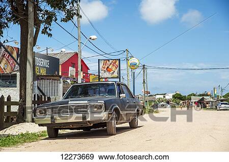 Vintage car parked on the dirt road outside colourful retail buildings; Valizas, Uruguay View Large Photo Image Stock Photo - Vintage car parked on the dirt road outside colourful retail buildings; Valizas, Uruguay. Fotosearch