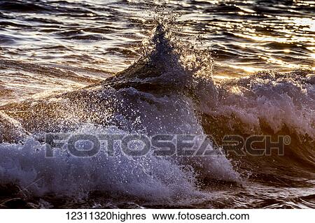 Stock Photograph - Wave crashing on the Kona coast at sunset; Kona, Island of Hawaii, Hawaii, United States of America. Fotosearch