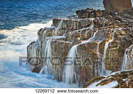 Stock Image - Wave splashes on lava cliffs creating silky waterfalls under the warm afternoon sun; Island of Hawaii, Hawaii, United States of America. Fotosearch
