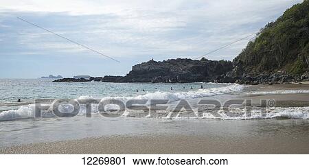 Stock Image - Waves crash into the beach and swimmers in the water; Guerrero, Mexico. Fotosearch