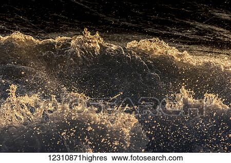 Stock Photograph - Waves crashing on the Kona coast at sunset; Kona, Island of Hawaii, Hawaii, United States of America. Fotosearch