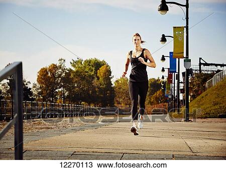 Stock Image - Woman going for a run along a sidewalk in autumn; Montreal, Quebec, Canada. Fotosearch