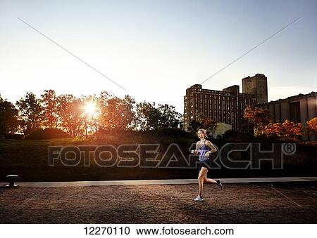 Stock Image - Woman going for a run through a park in autumn; Montreal, Quebec, Canada. Fotosearch