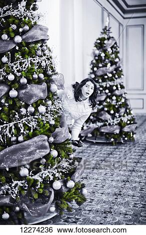 Stock Photograph - Woman peeking around Christmas tree in lobby; Vancouver, British Columbia, Canada. Fotosearch