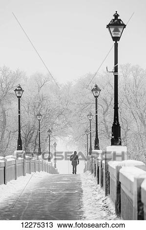 Stock Image - Woman walking across the Assiniboine Park foot bridge in winter; Winnipeg, Manitoba, Canada. Fotosearch