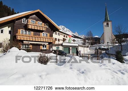Stock Photograph - Wooden house and village church with drifts of snow and mountain peaks; Filzmoos, Austria. Fotosearch