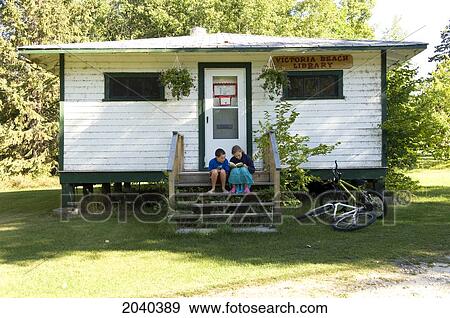 Stock Photo - Young Boy And Girl Reading Book Outside Community Library, Victoria Beach, Manitoba. Fotosearch