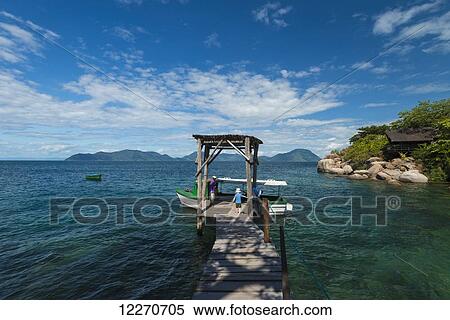 Stock Photography - Young boy walking along narrow wooden jetty to boat off Mumbo Island, Lake Malawi; Malawi. Fotosearch