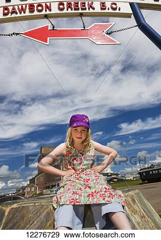 Stock Photo - Young girl sits under the Alaska Highway mile zero sign, Dawson Creek, British, Canada. Fotosearch