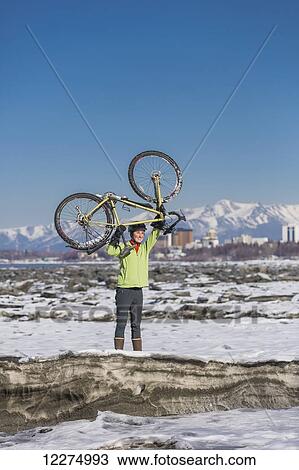 Young woman holding her bicycle over her head stands on frozen ice chunks along the Tony Knowles Coastal Trail, Anchorage, Southcentral Alaska View Large Photo Image Stock Image - Young woman holding her bicycle over her head stands on frozen ice chunks along the Tony Knowles Coastal Trail, Anchorage, Southcentral Alaska. Fotosearch
