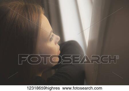 Stock Photograph - Young woman looking out a window; Connecticut, United States of America. Fotosearch