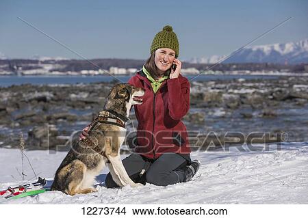 Young woman with her Alaska Husky talks on a cell phone along the Tony Knowles Coastal Trail, Anchorage, Southcentral Alaska View Large Photo Image Picture - Young woman with her Alaska Husky talks on a cell phone along the Tony Knowles Coastal Trail, Anchorage, Southcentral Alaska. Fotosearch