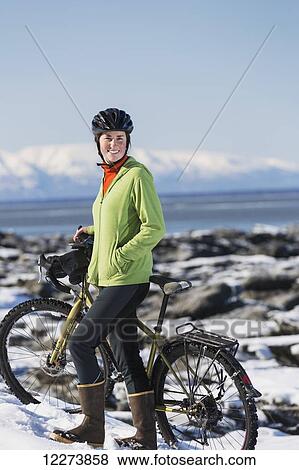 Stock Photo - Young woman with her bicycle stands on frozen ice chunks along the Tony Knowles Coastal Trail, Anchorage, Southcentral Alaska. Fotosearch
