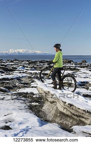 Young woman with her bicycle stands on frozen ice chunks along the Tony Knowles Coastal Trail, Anchorage, Southcentral Alaska View Large Photo Image Stock Photography - Young woman with her bicycle stands on frozen ice chunks along the Tony Knowles Coastal Trail, Anchorage, Southcentral Alaska. Fotosearch