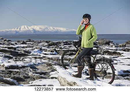 Young woman with her bicycle talks on a cell phone while standing on frozen ice chunks along the Tony Knowles Coastal Trail, Anchorage, Southcentral Alaska View Large Photo Image Stock Photo - Young woman with her bicycle talks on a cell phone while standing on frozen ice chunks along the Tony Knowles Coastal Trail, Anchorage, Southcentral Alaska. Fotosearch