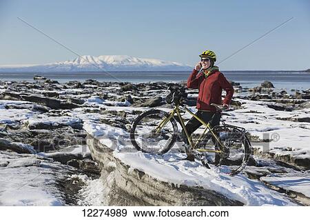 Young woman with her bicycle talks on a cell phone while standing on frozen ice chunks along the Tony Knowles Coastal Trail, Anchorage, Southcentral Alaska View Large Photo Image Stock Photo - Young woman with her bicycle talks on a cell phone while standing on frozen ice chunks along the Tony Knowles Coastal Trail, Anchorage, Southcentral Alaska. Fotosearch
