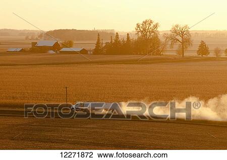 Stock Image - A grain truck hauls newly harvested grain along a dusty country road in late afternoon light, near Blue Earth; Minnesota, United States of America. Fotosearch