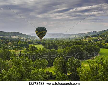 Stock Photo - A hot air balloon flies low over a spring valley landscape; Tuscany, Italy. Fotosearch
