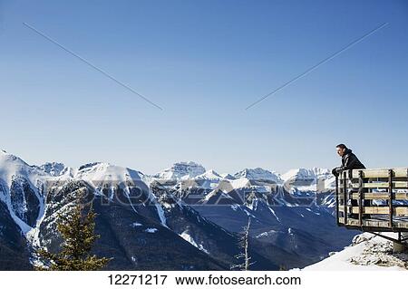 Stock Photo - A man stands with a view from Sulphur mountain of the Canadian Rockies in winter; Banff, Alberta, Canada. Fotosearch