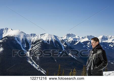 Stock Photograph - A man stands with a view from Sulphur mountain of the Canadian Rockies in winter; Banff, Alberta, Canada. Fotosearch
