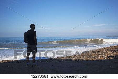 Stock Image - A man watches the swell crash on the beach; Puerto Vallarta, Mexico. Fotosearch