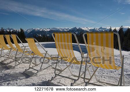 A row of yellow and white striped deck chairs waits for customers in the sunshine outside a cafe at the top of a ski piste with views of across the mountain peaks of the Austrian Alps; Filzmoos, Austria View Large Photo Image Stock Photo - A row of yellow and white striped deck chairs waits for customers in the sunshine outside a cafe at the top of a ski piste with views of across the mountain peaks of the Austrian Alps; Filzmoos, Austria. Fotosearch