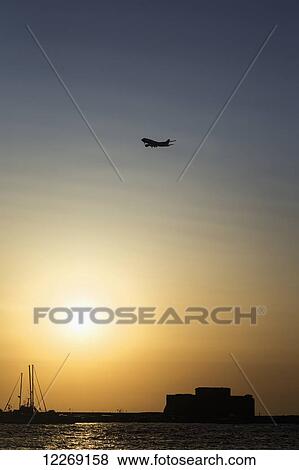 Airplane flying over the harbour at sunset; Paphos, Cyprus View Large Photo Image Stock Photo - Airplane flying over the harbour at sunset; Paphos, Cyprus. Fotosearch