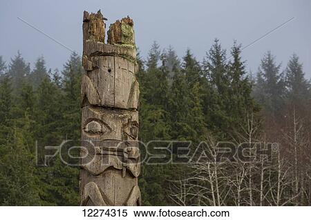 Stock Photography - An old carved wooden totem pole with a forest and fog; British Columbia, Canada. Fotosearch
