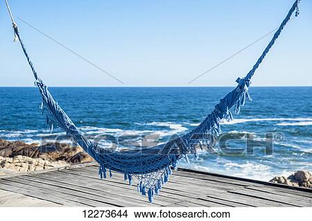 Picture - Blue hammock over a wooden dock at the water's edge; Cabo Polonio, Uruguay. Fotosearch