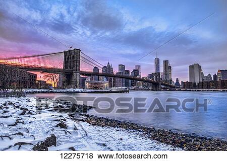 Stock Photo - Brooklyn Bridge with snow-covered landscape at sunset, Brooklyn Bridge Park; Brooklyn, New York, United States of America. Fotosearch