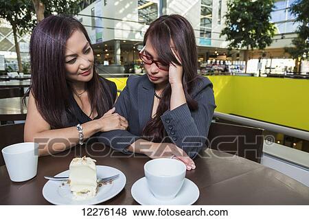 Businesswoman comforting her distraught friend in a coffee shop at a shopping complex; St. Albert, Alberta, Canada View Large Photo Image Stock Photo - Businesswoman comforting her distraught friend in a coffee shop at a shopping complex; St. Albert, Alberta, Canada. Fotosearch