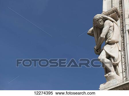 Stock Photography - Carved sculpture of male likeness on the facade of Milan Cathedral against a blue sky; Milan, Lombardy, Italy. Fotosearch